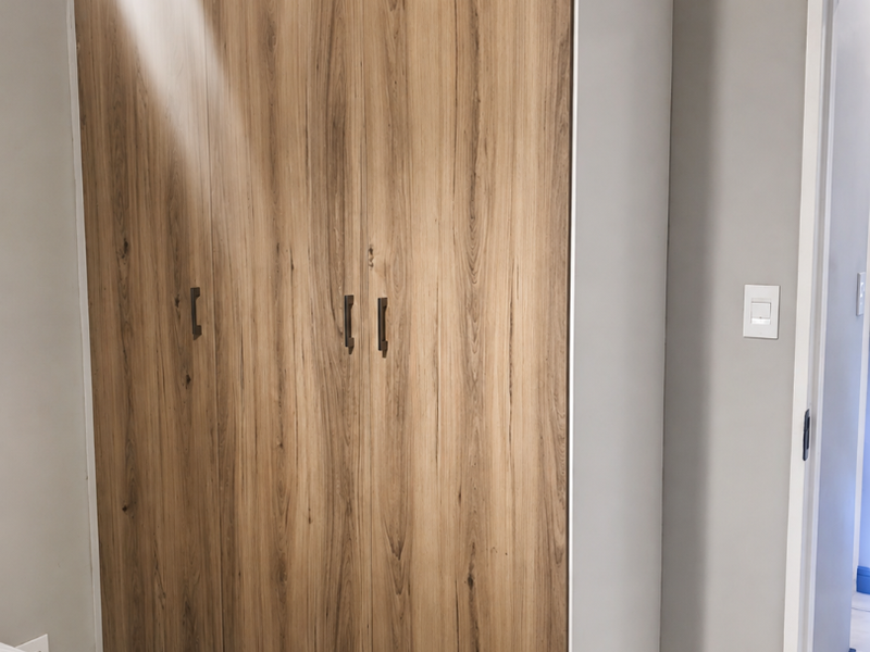 A bedroom featuring a modern wood-finish built-in wardrobe with dark hardware, tiled flooring, and neutral wall tones.