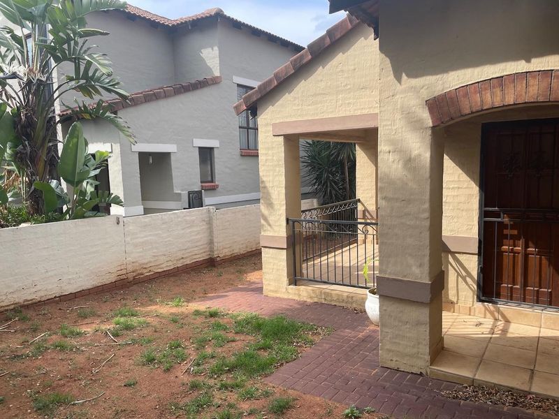 A rear exterior view featuring a covered patio with wrought iron railings, brick paving, and a small garden area with a boundary wall.