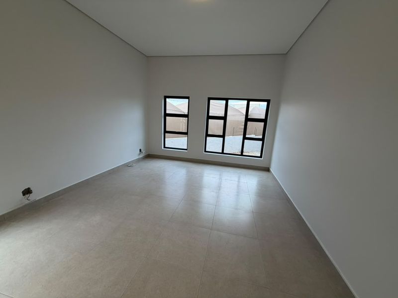 A bright, empty bedroom featuring neutral tiled flooring and modern black-framed windows, offering a clean and versatile space ready for personalization.
