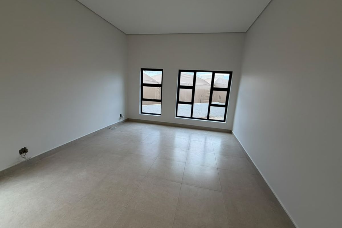 A bright, empty bedroom featuring neutral tiled flooring and modern black-framed windows, offering a clean and versatile space ready for personalization.