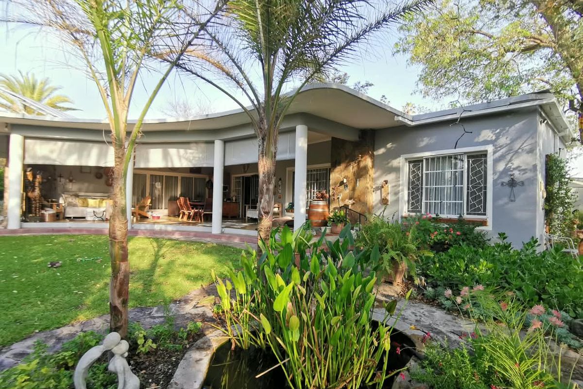 Rear view of the house featuring a covered patio, landscaped garden, and a stone-lined pond.