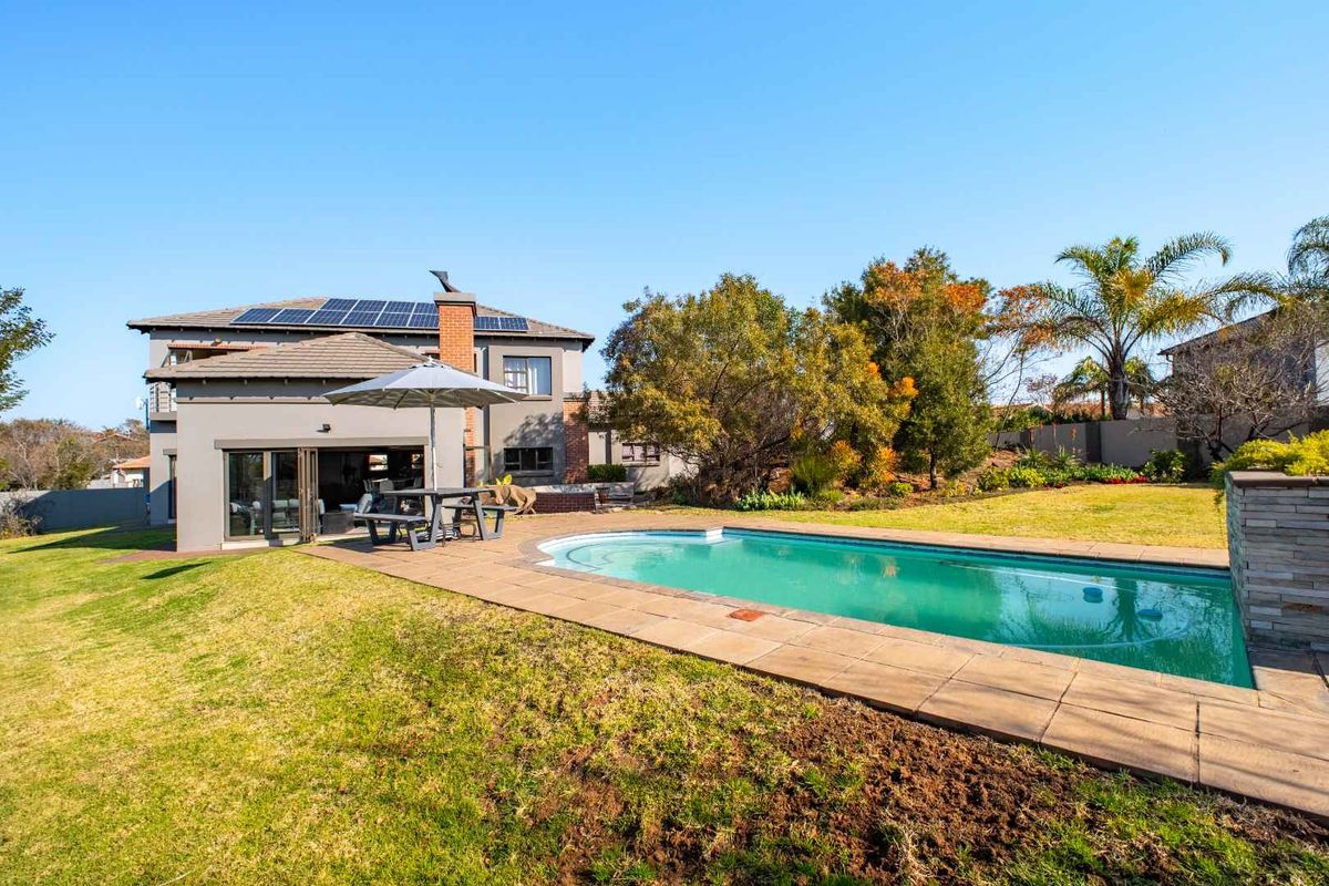 Rear view of the property featuring a swimming pool, paved patio area, landscaped garden, and solar panels installed on the tiled roof.