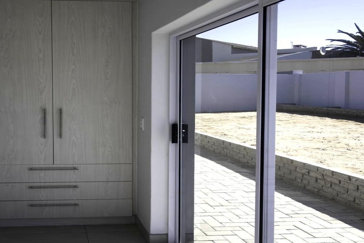 A bright interior space featuring built-in light wood cabinetry and large sliding glass doors that open onto a paved patio and rear garden area.
