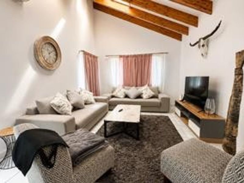 A bright and spacious living room featuring a high vaulted ceiling with exposed timber beams and neutral tiled flooring.