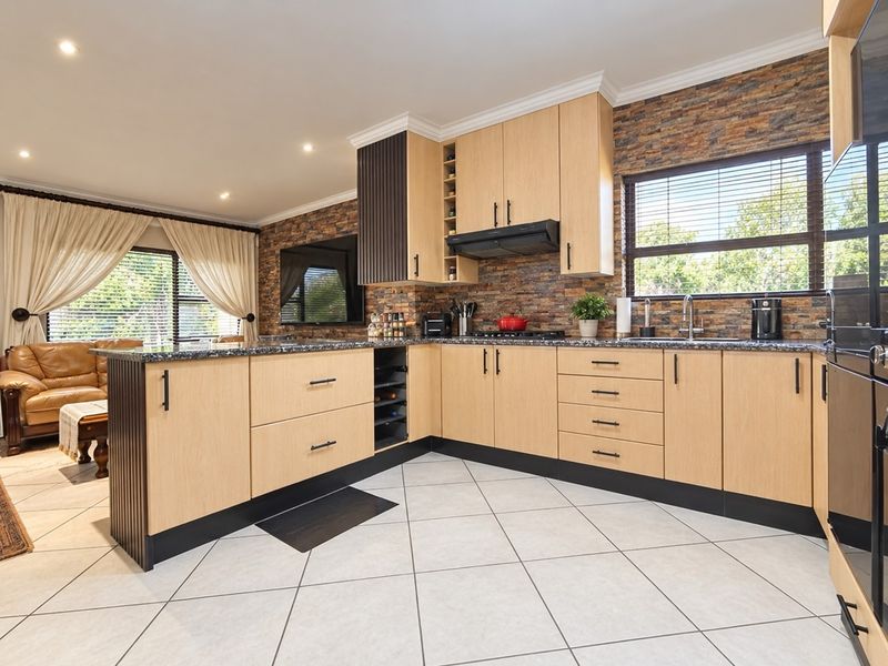 Modern open-plan kitchen featuring light wood cabinetry, granite countertops, stone veneer accents, and integrated appliances, seamlessly flowing into the adjacent living area.