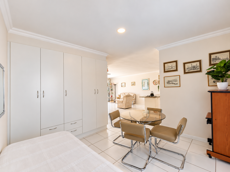 An open-plan living and dining area featuring neutral tiled flooring, extensive built-in wardrobe storage, and recessed ceiling lighting, flowing into the adjacent living space.