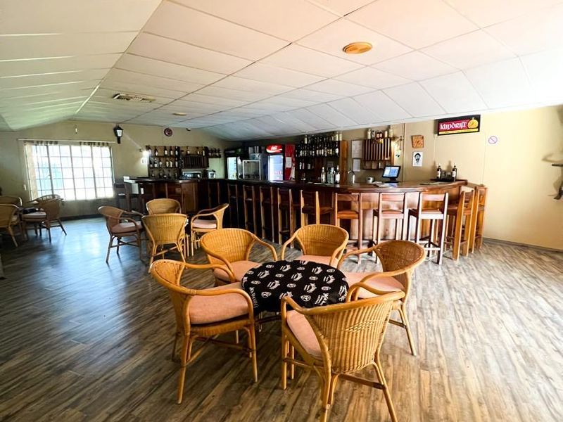 A spacious hotel bar area featuring a long built-in service counter, wood-look flooring, and a suspended ceiling.