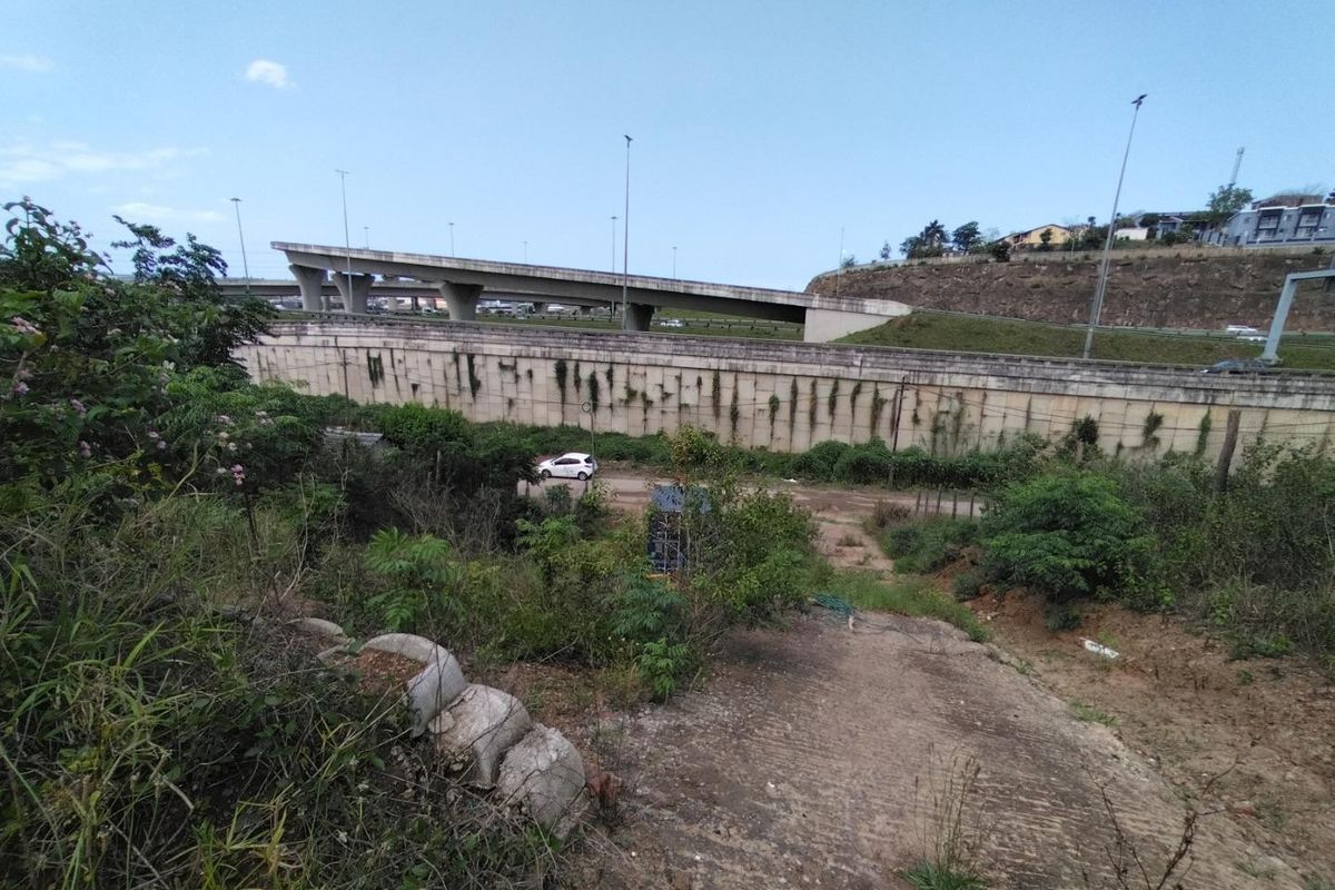 View of the rear land area featuring a concrete retaining wall and driveway, situated adjacent to a highway overpass.