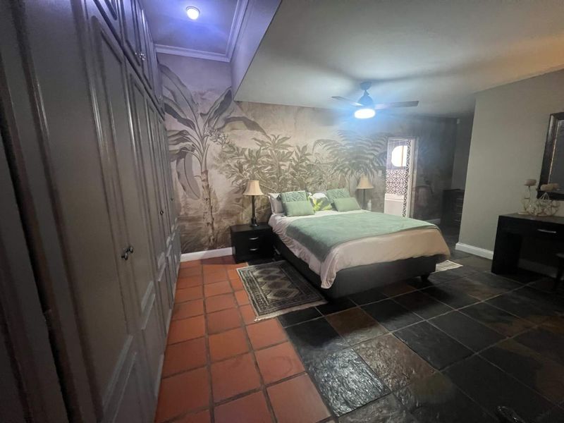 Spacious bedroom featuring a mix of terracotta and slate flooring, extensive built-in cabinetry, and a decorative mural wall with an integrated ceiling fan.