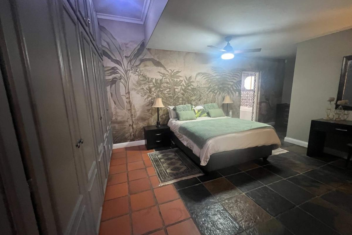Spacious bedroom featuring a mix of terracotta and slate flooring, extensive built-in cabinetry, and a decorative mural wall with an integrated ceiling fan.