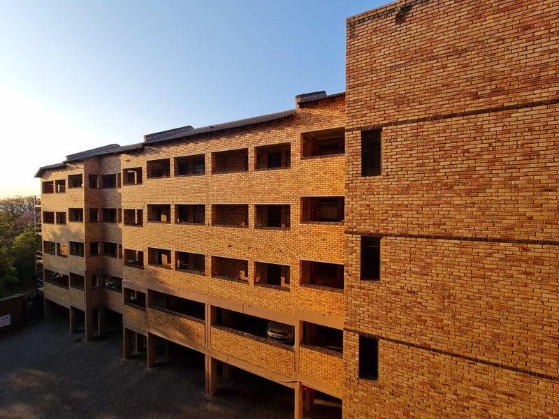 Exterior view of a multi-story apartment building featuring a face brick facade, integrated covered balconies, and ground-level undercover parking.