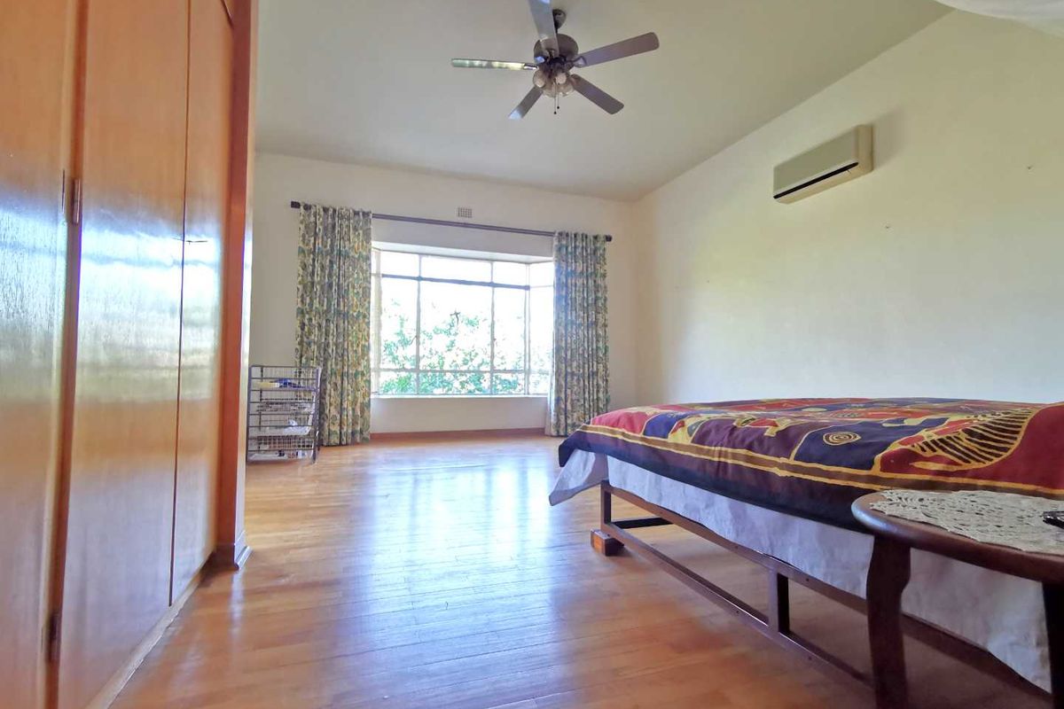 Spacious bedroom featuring polished timber flooring, built-in wooden cabinetry, a ceiling fan, and a wall-mounted air conditioning unit.
