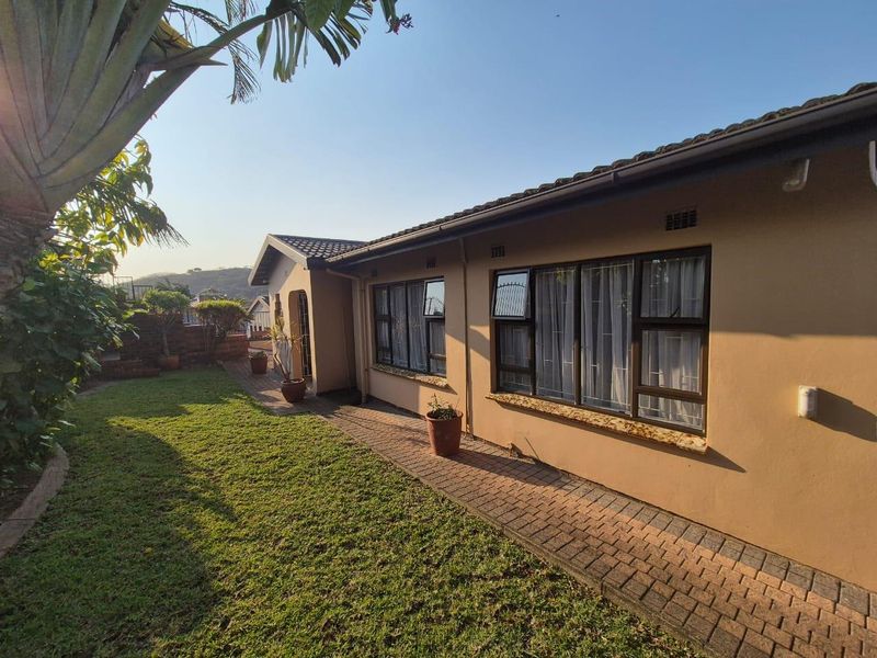 A well-maintained rear exterior view of the house featuring a brick paved walkway, lawn, and aluminium window frames with security bars.