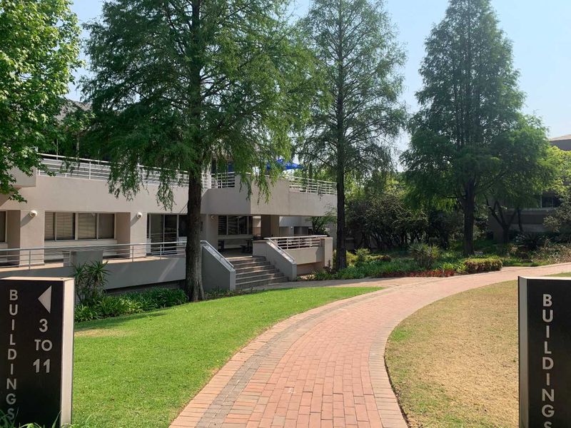 A well-maintained office park exterior featuring paved walkways, landscaped gardens, and modern building facades with balcony access.