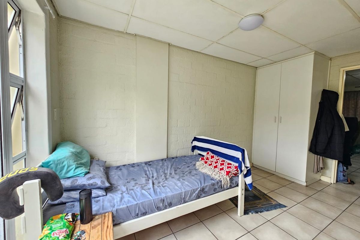 A bedroom featuring built-in cupboards, tiled flooring, and a drop ceiling, offering a functional space with potential for cosmetic updates.