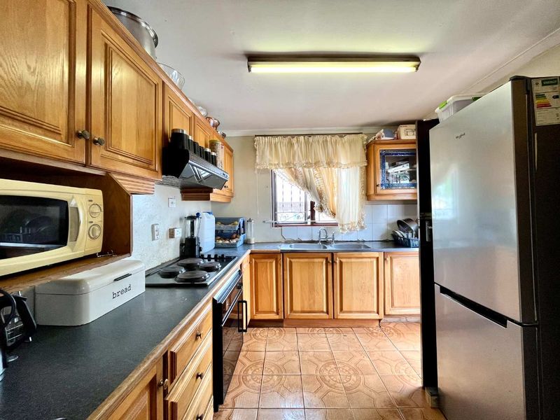 A functional kitchen featuring traditional wooden cabinetry, laminate countertops, a built-in oven with hob, and tiled flooring.