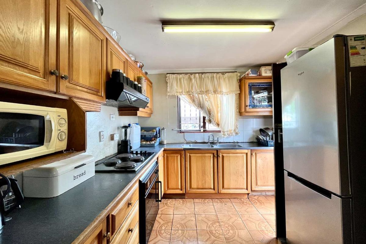 A functional kitchen featuring traditional wooden cabinetry, laminate countertops, a built-in oven with hob, and tiled flooring.