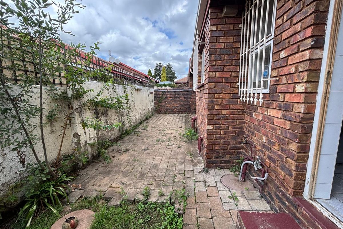 A side exterior area featuring brick paving, a face-brick townhouse wall, and a boundary wall requiring maintenance and landscaping.