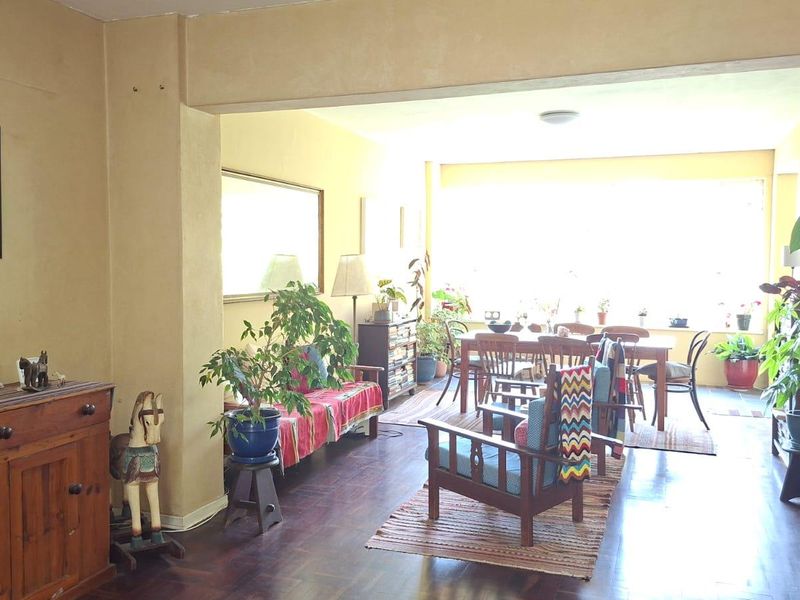 Spacious open-plan living and dining area featuring warm-toned parquet flooring and large windows that provide ample natural light.