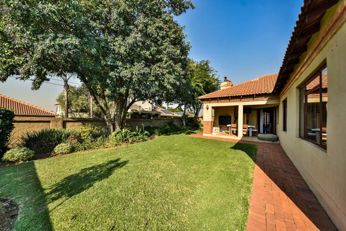 A well-maintained rear garden featuring a covered patio, brick-paved walkway, and established lawn, enclosed by a solid boundary wall.