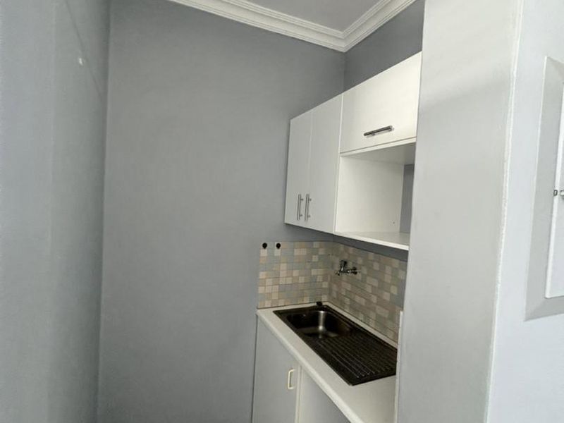 A compact, functional scullery area featuring built-in white cabinetry, a stainless steel sink, and a tiled backsplash.
