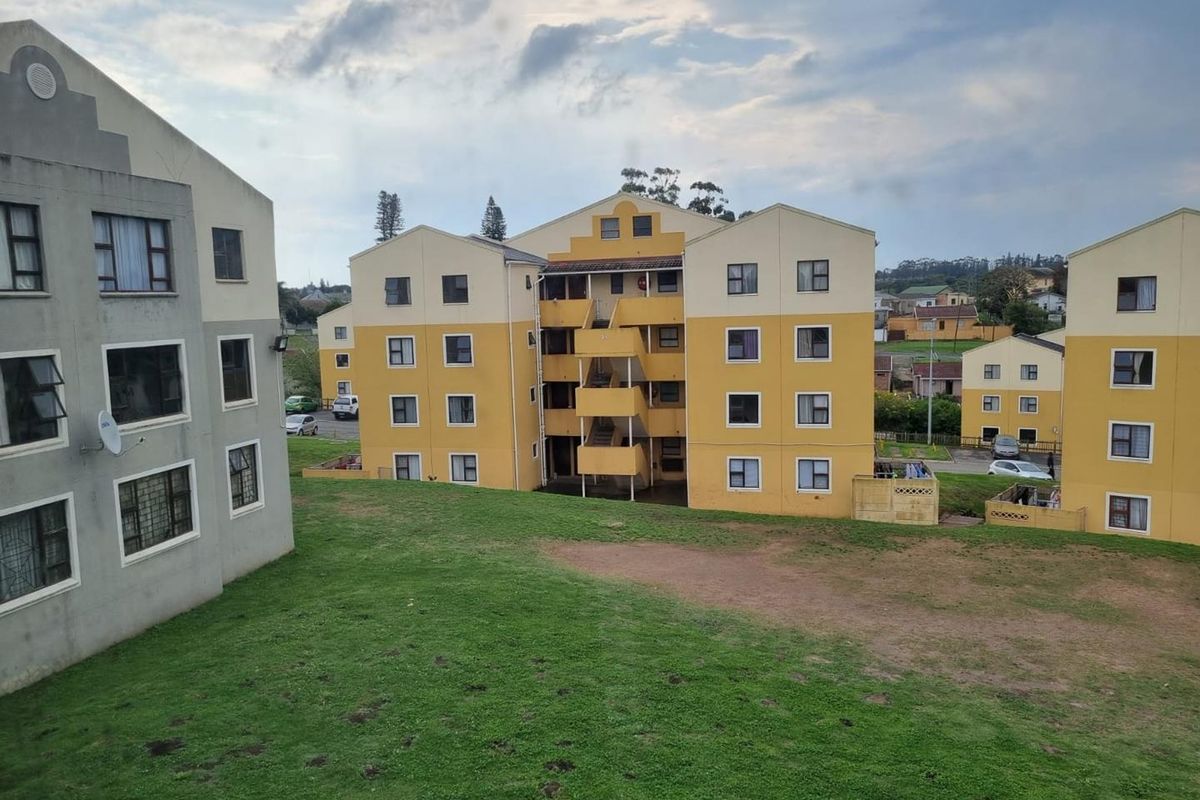 View of multi-story apartment blocks featuring external staircases and communal green space in a residential complex.