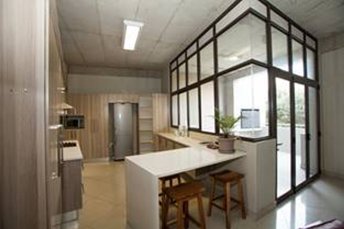 Modern kitchen featuring sleek cabinetry, stone breakfast bar, and an industrial-style exposed concrete ceiling with a glass partition wall.