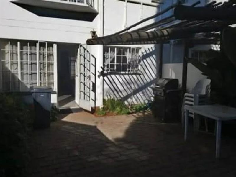 Rear exterior view of the townhouse featuring a paved patio area with a timber pergola and security-barred windows.