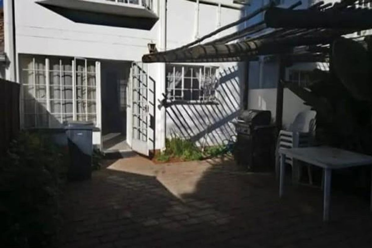 Rear exterior view of the townhouse featuring a paved patio area with a timber pergola and security-barred windows.