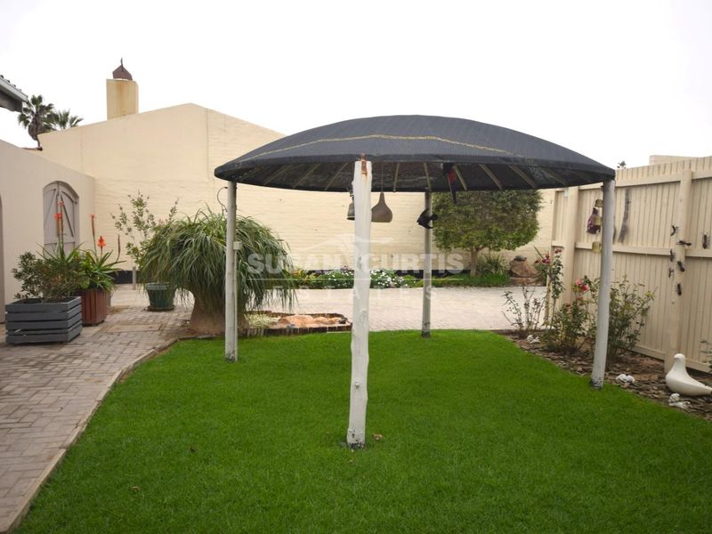 A rear garden area featuring a lawn, paved walkway, timber fencing, and a central gazebo structure.