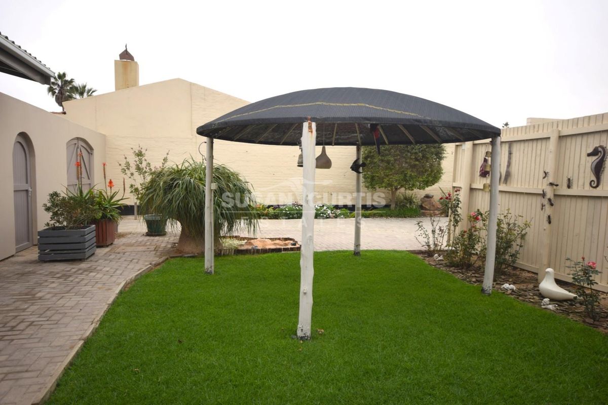 A rear garden area featuring a lawn, paved walkway, timber fencing, and a central gazebo structure.