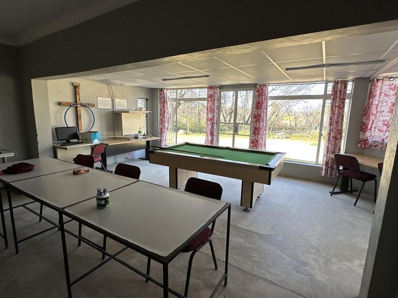 A spacious multi-purpose room featuring large glass sliding doors, concrete flooring, and a suspended ceiling, offering potential for a versatile living or entertainment area.