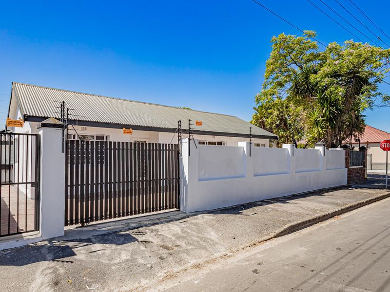 Front exterior view of the property featuring a secure perimeter wall with electric fencing, a metal driveway gate, and a corrugated metal roof.