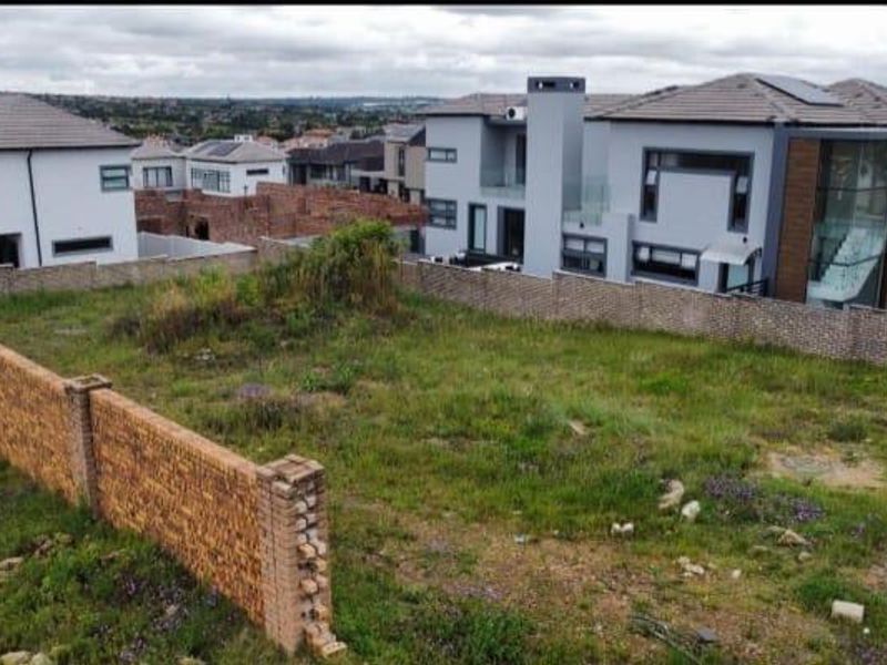 A vacant residential plot of land enclosed by a brick boundary wall, situated in a developed suburban estate.