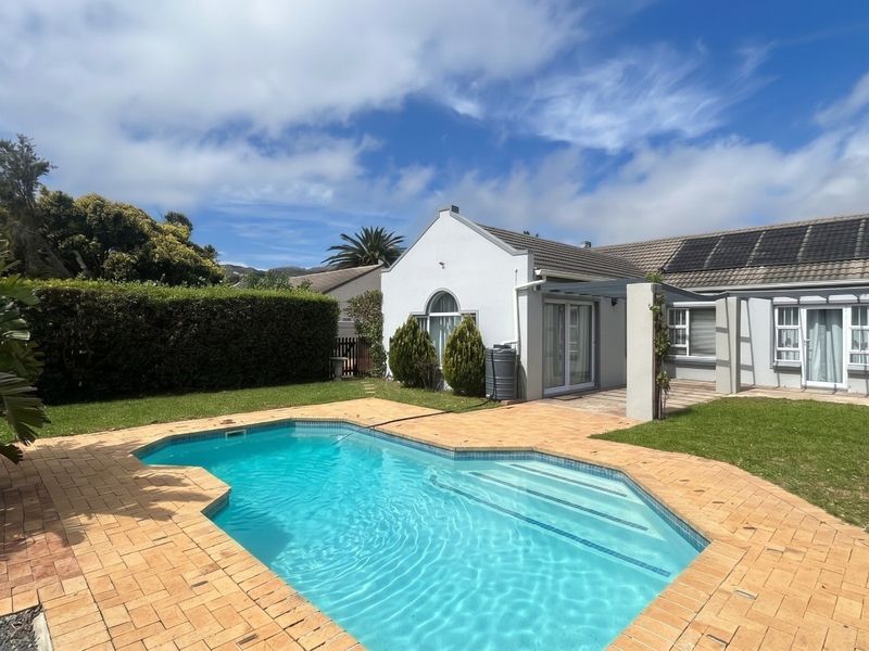 A well-maintained rear garden featuring a swimming pool, paved surround, covered patio area, and solar panels installed on the roof.
