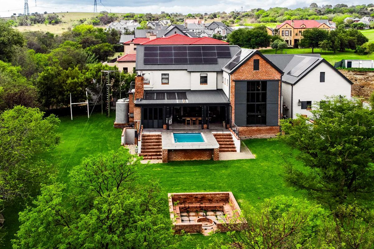 Aerial view of a modern residential property featuring a swimming pool, brick fire pit, solar panels, and a spacious landscaped garden.