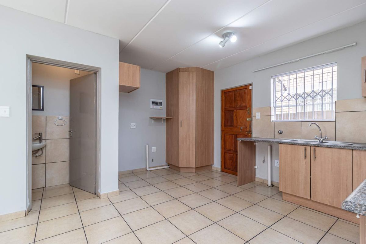 A functional kitchen area featuring light wood-finish cabinetry, tiled flooring, and a built-in sink, with an adjacent doorway leading to a small bathroom.