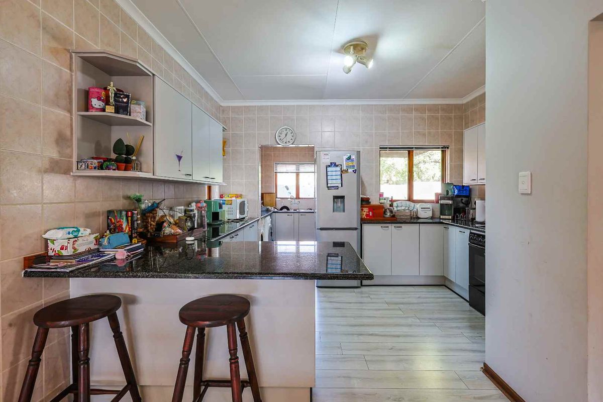 A functional kitchen featuring granite countertops, built-in cabinetry, and a breakfast bar, with an adjoining scullery area visible in the background.