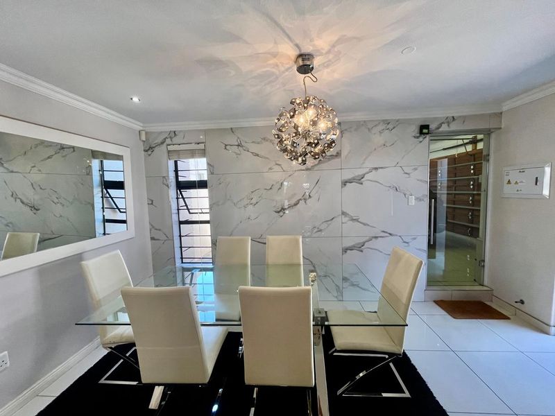 Modern dining room featuring elegant marble-look wall cladding, polished tiled flooring, and a striking contemporary pendant light fixture.