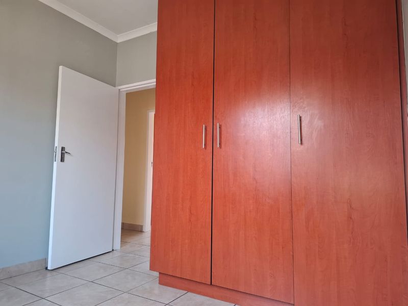 A bedroom featuring tiled flooring and a large built-in wooden wardrobe, leading into a hallway.