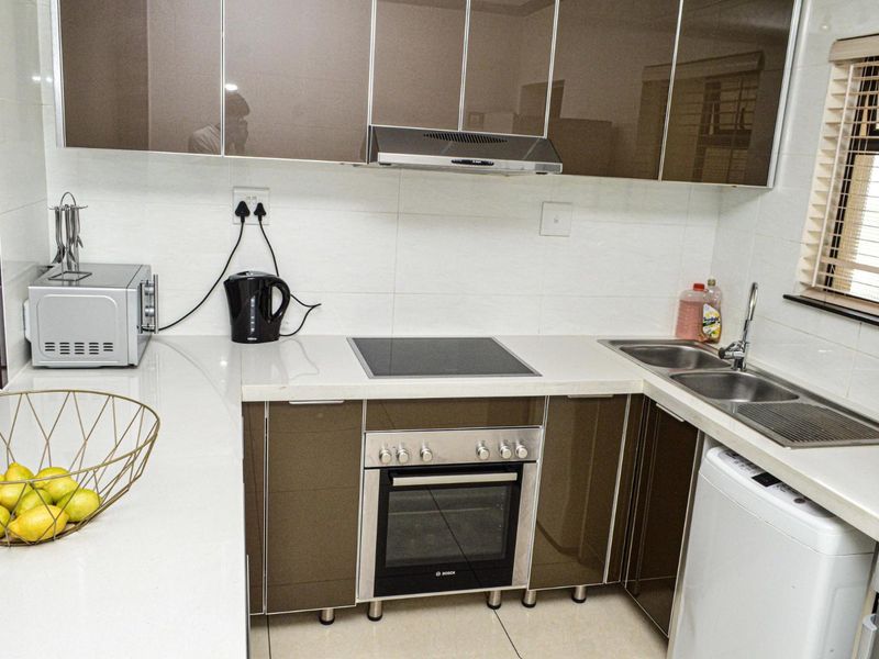 Modern kitchen featuring high-gloss cabinetry, stone countertops, integrated electric hob and oven, extractor fan, and a double basin sink with tiled finishes.
