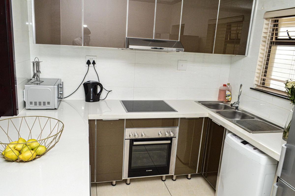 Modern kitchen featuring high-gloss cabinetry, stone countertops, integrated electric hob and oven, extractor fan, and a double basin sink with tiled finishes.