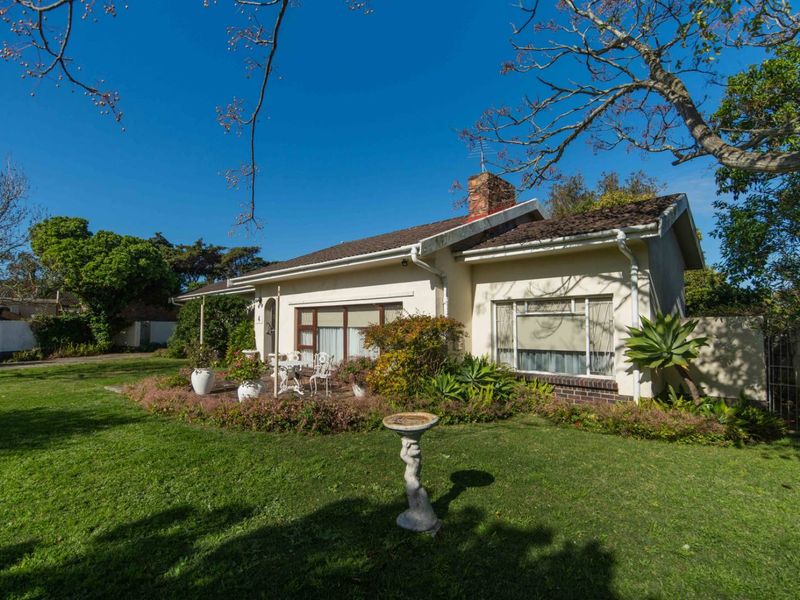 A view of the rear exterior of the house featuring a brick chimney, tiled roof, and a paved patio area set within a garden.