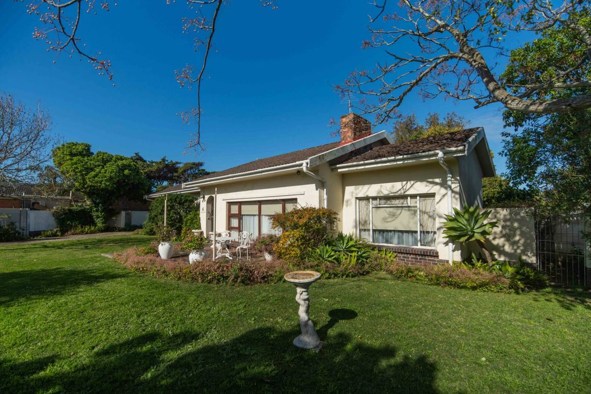 A view of the rear exterior of the house featuring a brick chimney, tiled roof, and a paved patio area set within a garden.