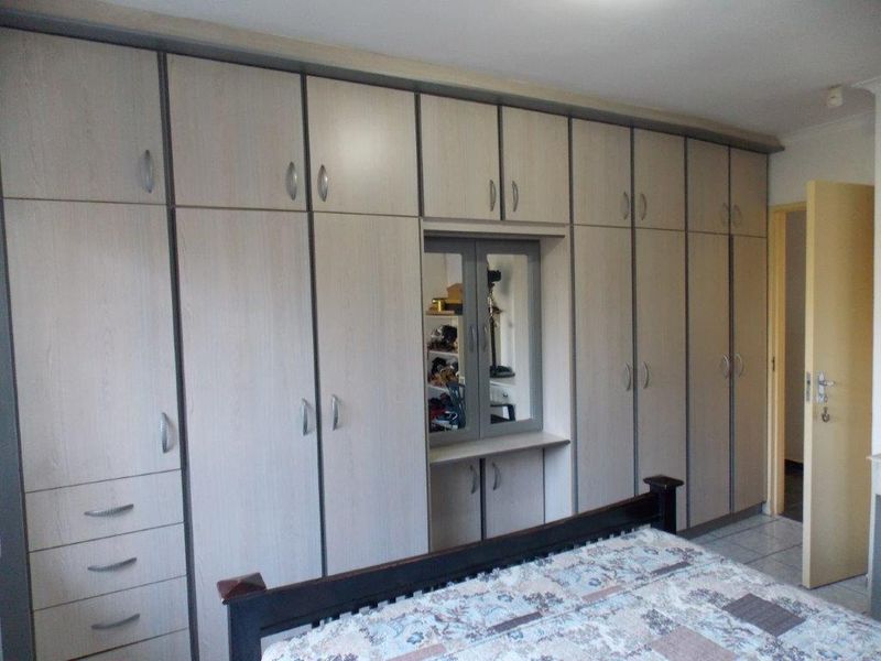 Bedroom featuring extensive wall-to-wall built-in cupboards with integrated vanity mirror and neutral wood-grain finish.