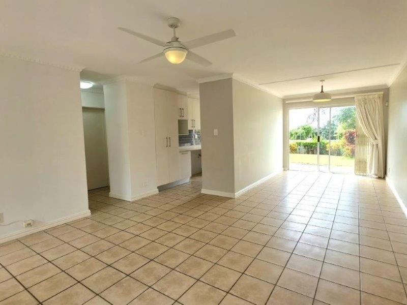 Spacious open-plan living and kitchen area featuring neutral tiled flooring, ceiling fans, and large sliding glass doors providing access to the garden.