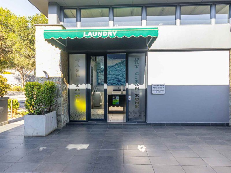 Exterior view of a commercial laundry and dry cleaning facility entrance featuring tiled flooring, stone cladding, and a green fabric awning.
