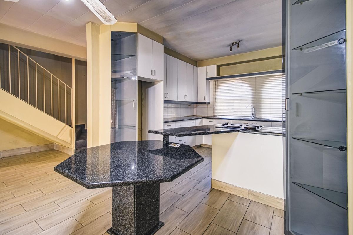 A functional kitchen featuring granite countertops, white cabinetry, a breakfast bar, and wood-look tiled flooring, adjacent to an internal staircase.