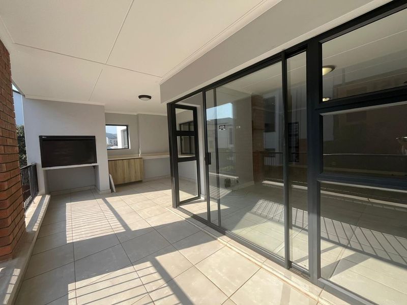 A spacious covered balcony featuring tiled flooring, a built-in braai, and modern sliding glass doors providing seamless access to the interior living space.