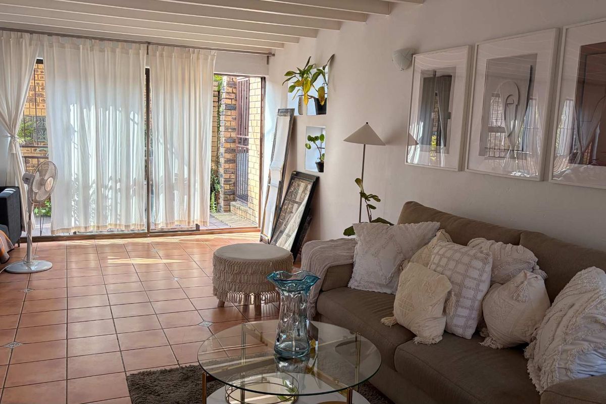 A bright living room featuring terracotta floor tiles, exposed beam ceilings, and a sliding glass door providing access to an outdoor area.